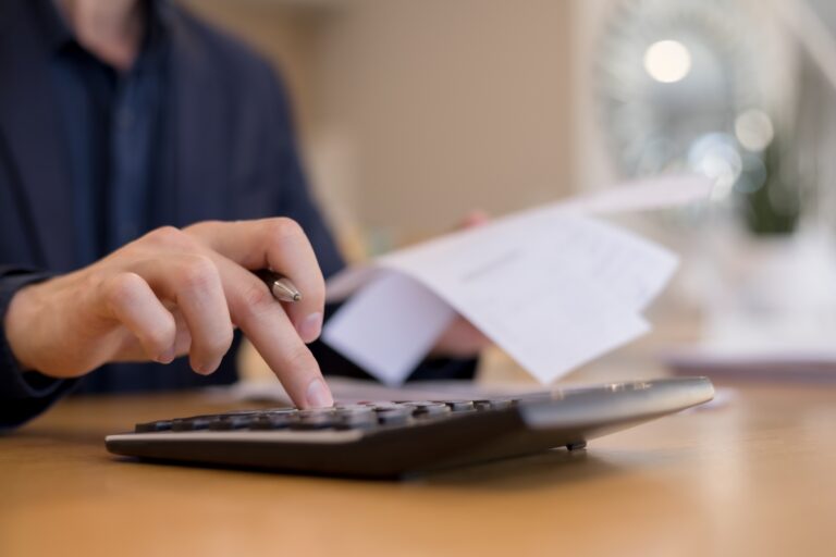 資料を手に持ち、電卓を使って計算するビジネスマンのクローズアップ