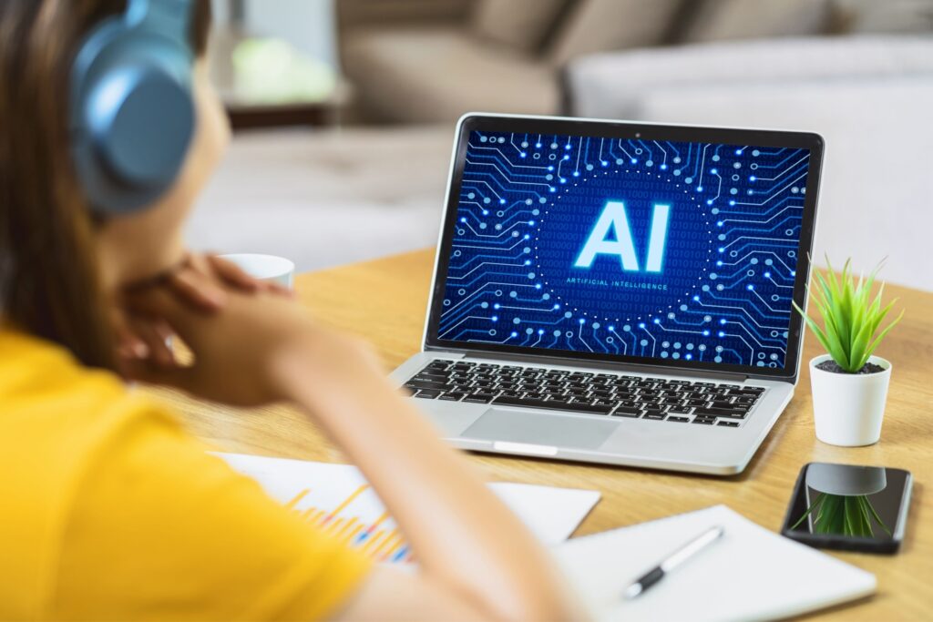 デスクで仕事・勉強をする若者。AIポータルへアクセス中のノートPC画面に、ネオンに光る「AI」の文字。観葉植物とスマートフォン。